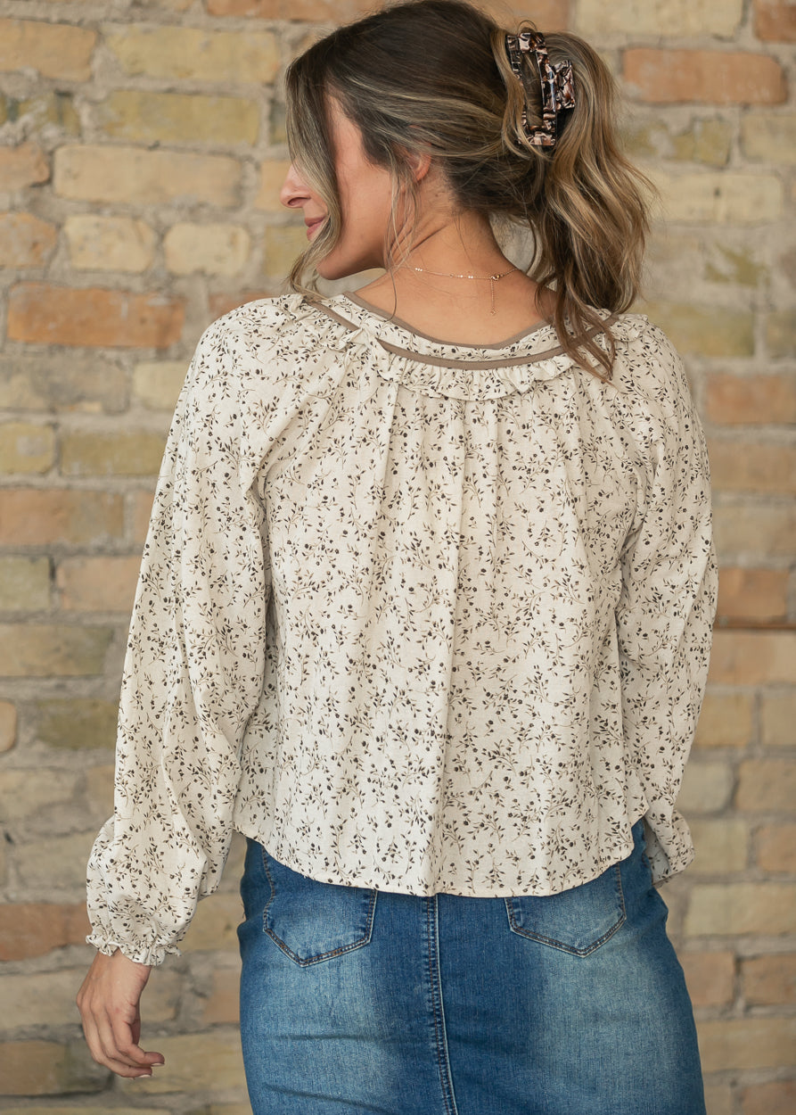 Back of cream botanical blouse showing gathered yoke, ruffle trim, and loose silhouette.