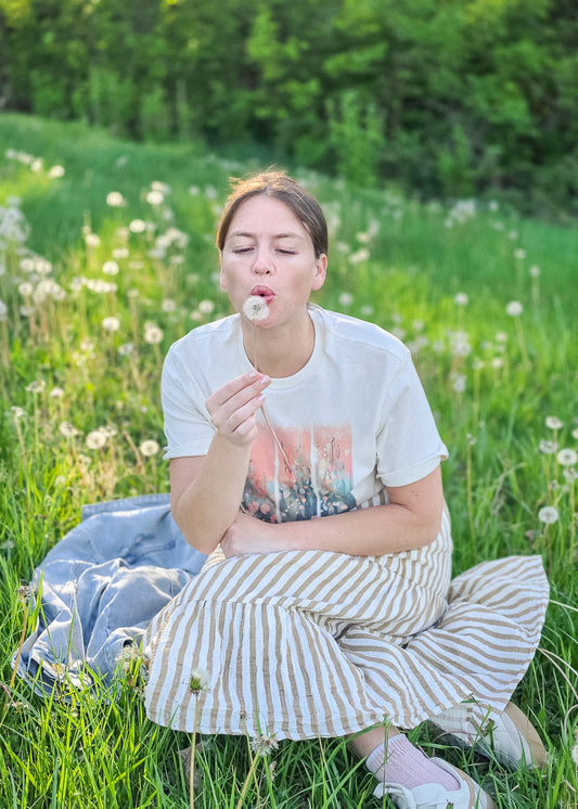 Woman sitting in a field blowing on dandelion seeds