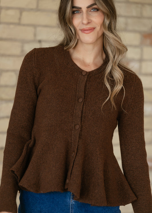 Brown knit peplum cardigan with a rounded neckline, matching front buttons, and long sleeves above a denim skirt.