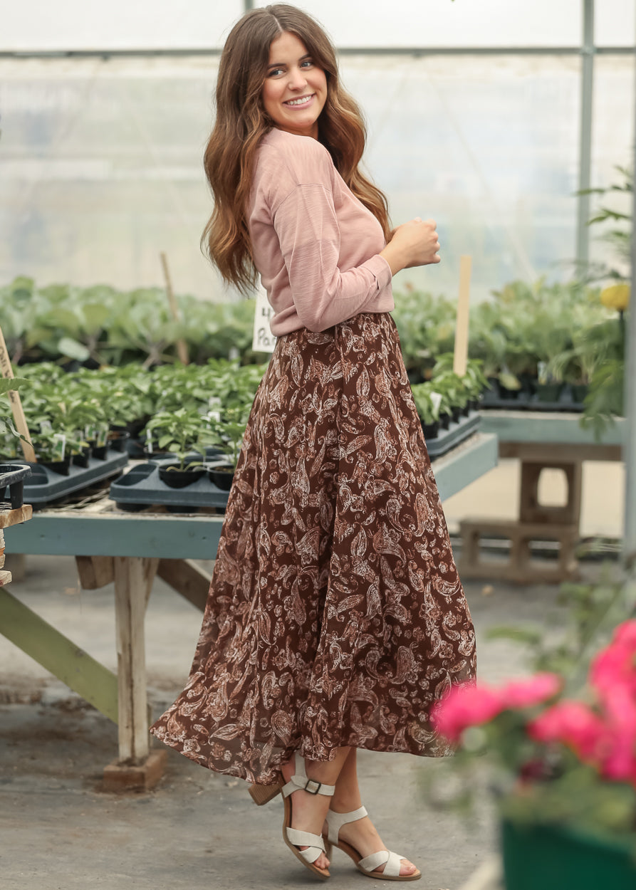 Mauve cropped cardigan paired with a flowing brown paisley maxi skirt and neutral heels