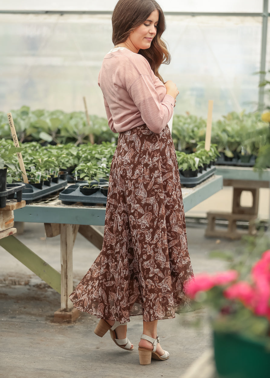 Mauve sheer knit cardigan styled with a brown paisley print skirt in a greenhouse