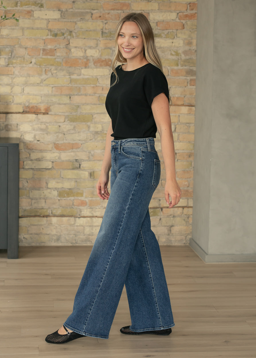 Black waist-length knit top paired with wide leg denim for everyday wear.