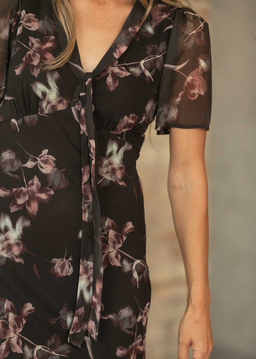 Close-up of charcoal floral maxi dress showing V-neckline, front tie, gathered waist, and sheer short sleeve.