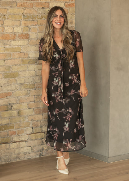 Charcoal floral maxi dress with V-neck tie detail and short sheer sleeves, styled with cream heels.