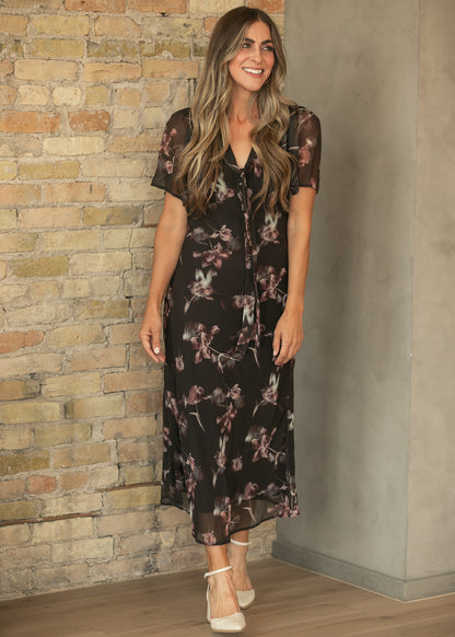 Charcoal floral V-neck maxi dress with front tie and ankle-length hem, styled with cream heels.