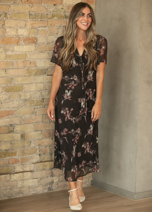 Charcoal floral V-neck maxi dress with front tie and ankle-length hem, styled with cream heels.