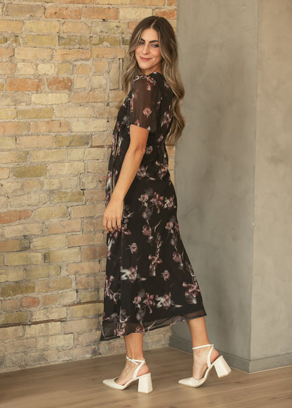 Side view of charcoal floral maxi dress with short sheer sleeves, fitted waist, and cream block heels.