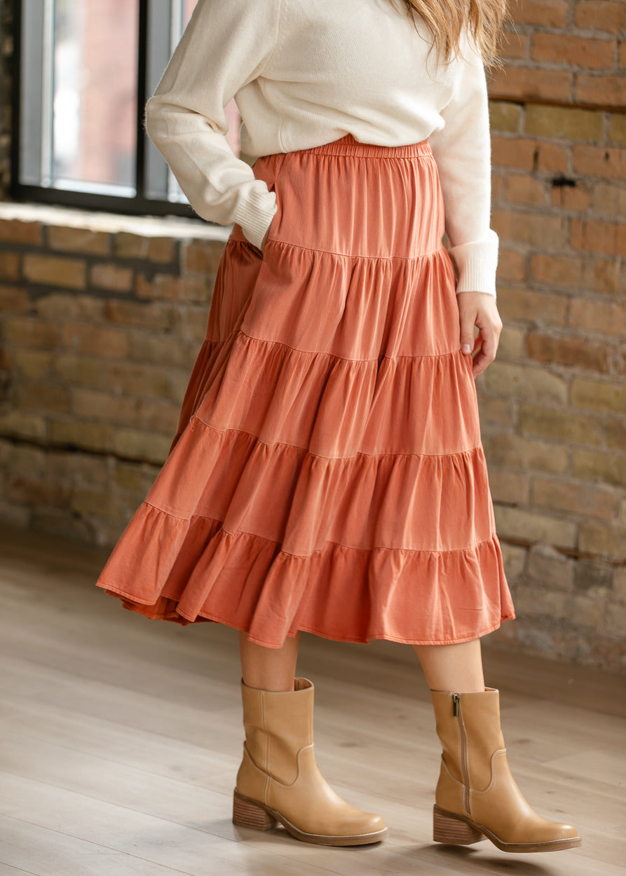 Washed rust midi skirt showing the softly gathered tiered silhouette and flowing hem.