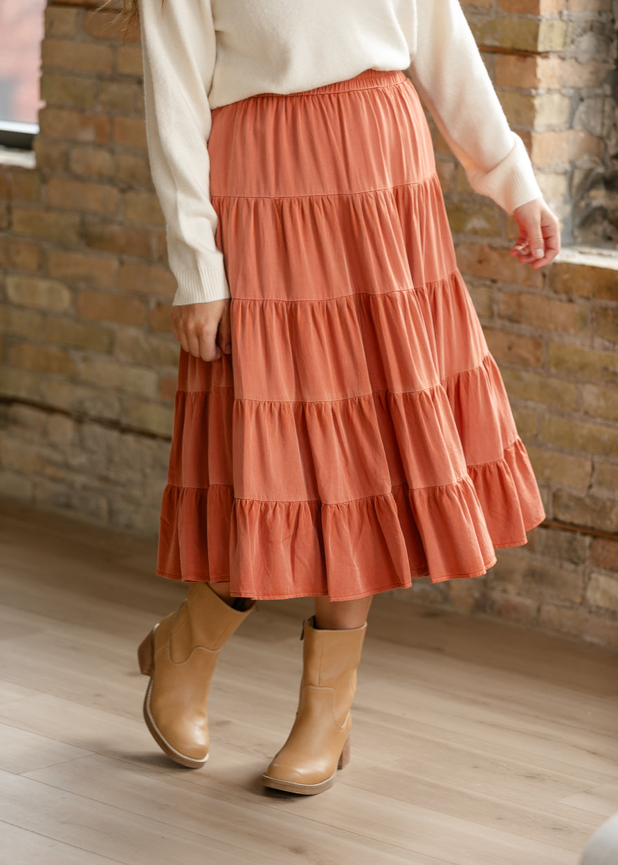 Flowy rust tiered midi skirt showing gathered tiers, midi length, and tan ankle boots.