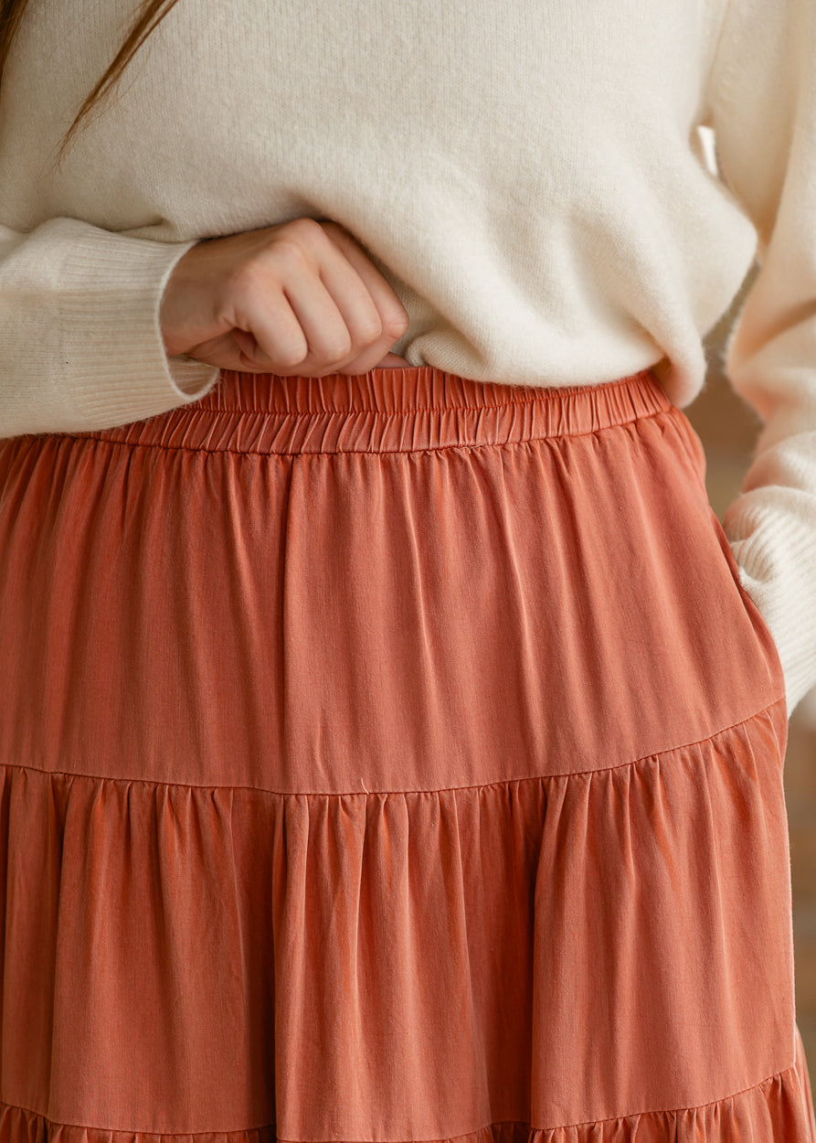 Close-up of the rust washed skirt showing the elastic waistband, tonal finish, and gathered first tier.