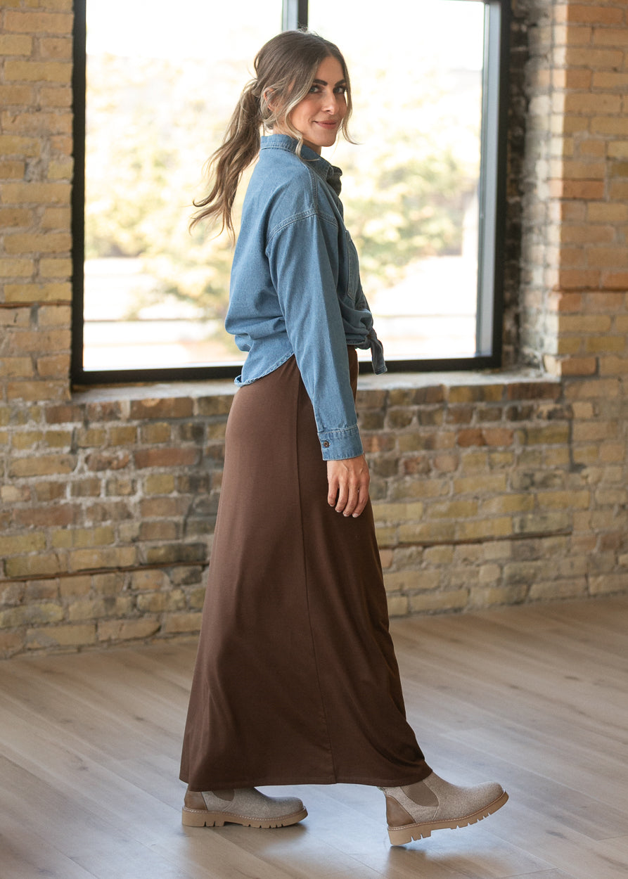 Chocolate brown maxi skirt in a side view, styled with a denim button-up and neutral ankle boots.