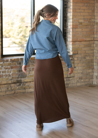 Back of the chocolate brown knit maxi skirt styled with a denim button-up and neutral ankle boots.