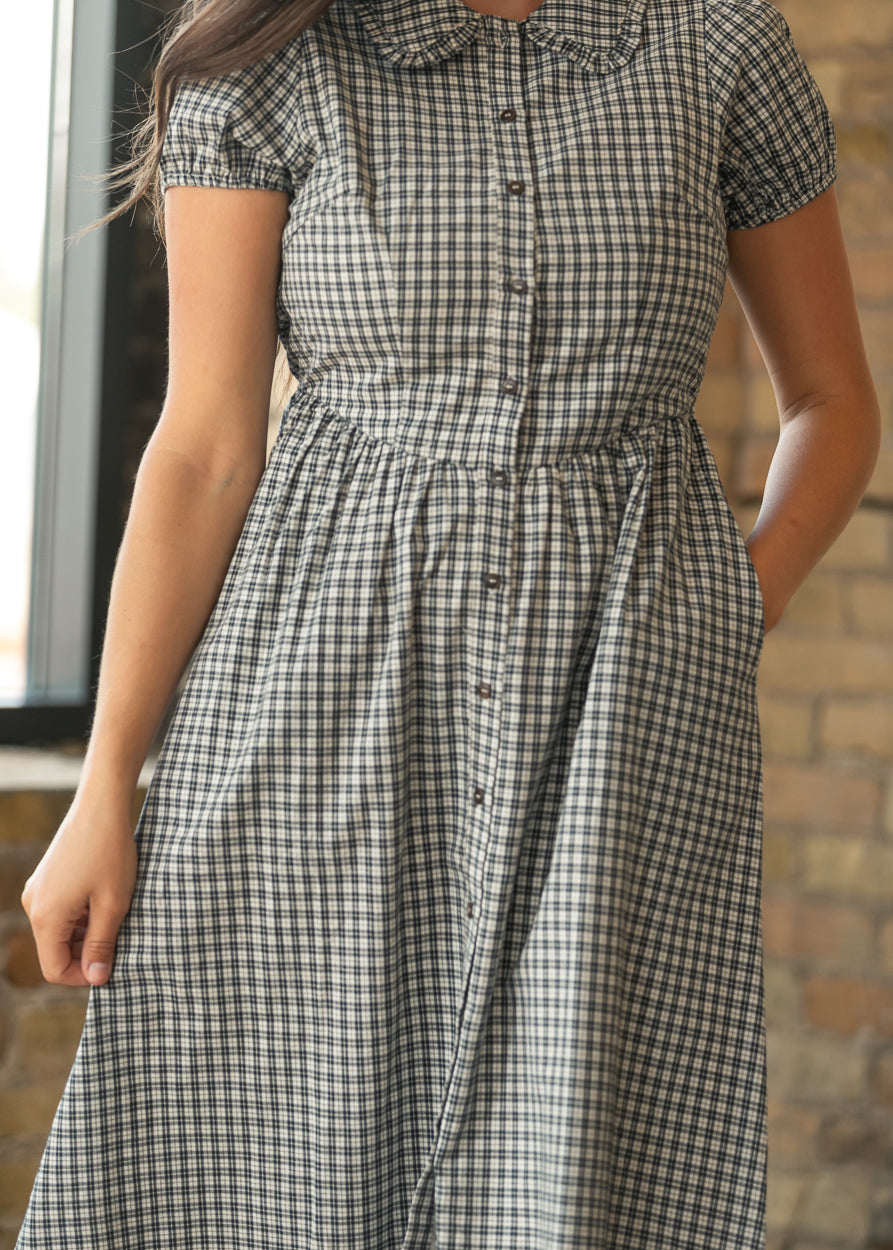 Close-up of dark navy gingham cotton midi dress showing gathered waist, button front, and side pocket.