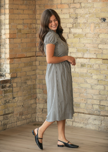 Side view of dark navy gingham midi dress with semi-fitted bodice, gathered skirt, and puff sleeves.