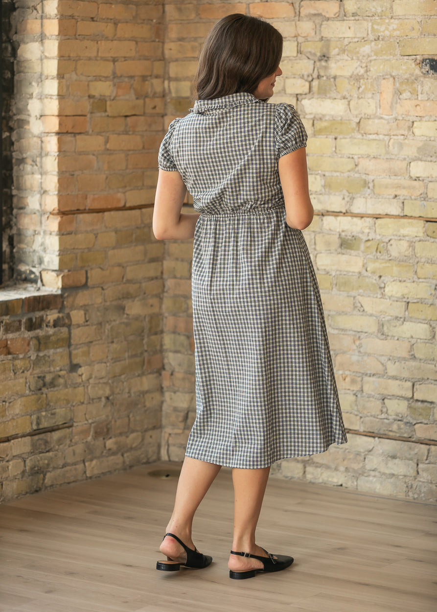 Back of dark navy gingham midi dress showing gathered waist, short puff sleeves, and below-knee hem.