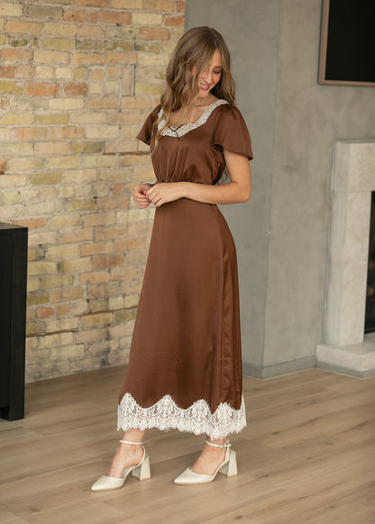 Chocolate brown midi dress with cream lace neckline and hem, shown with a flowing semi-fitted silhouette.