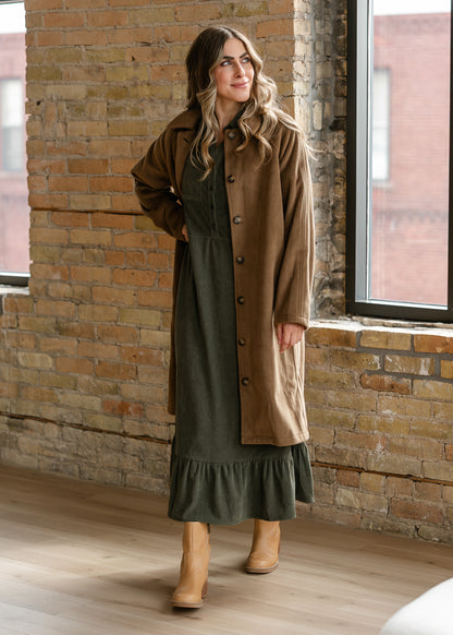 Olive corduroy midi dress layered under a long brown coat with tan ankle boots.
