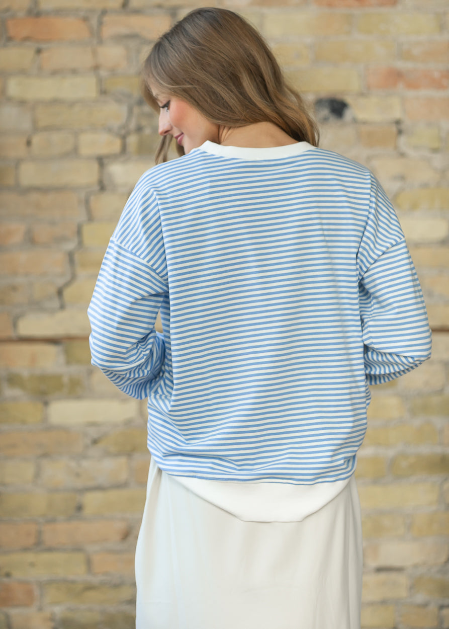 Back of cornflower blue striped crewneck sweater showing dropped shoulders and white contrast hem.