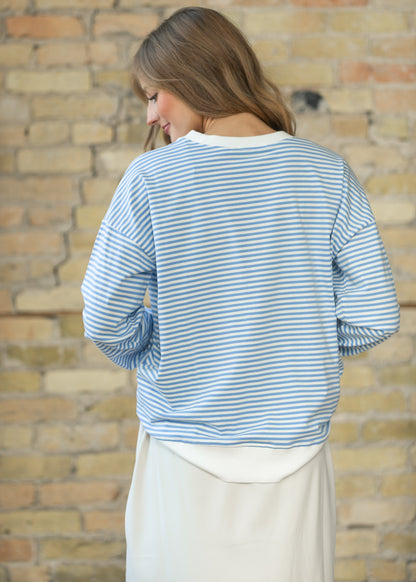 Back of cornflower blue striped crewneck sweater showing dropped shoulders and white contrast hem.