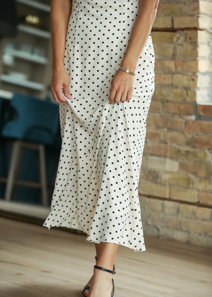 Close-up of cream polka-dot dress showing the flowing fabric and midi hem