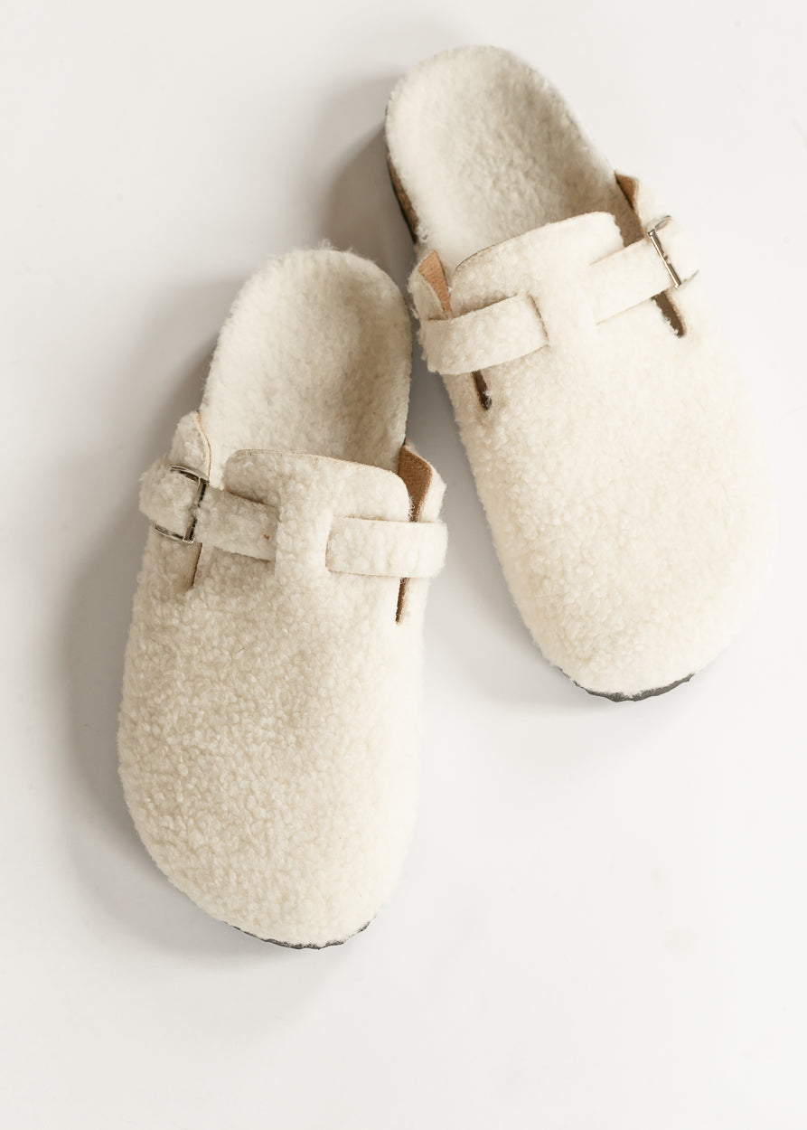 Ivory sherpa clogs with rounded toes, buckle straps, and fuzzy lining, photographed from above.
