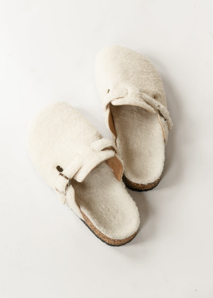Ivory sherpa clogs with silver-tone buckles and cork-look soles, angled studio view.