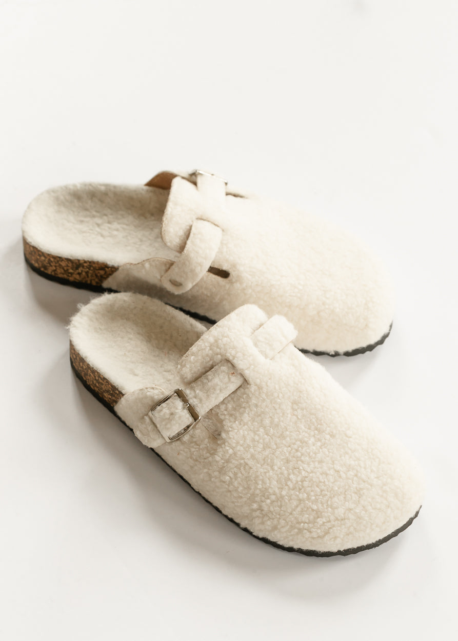 Top view of ivory sherpa clogs showing fuzzy footbeds, buckle straps, and open backs.