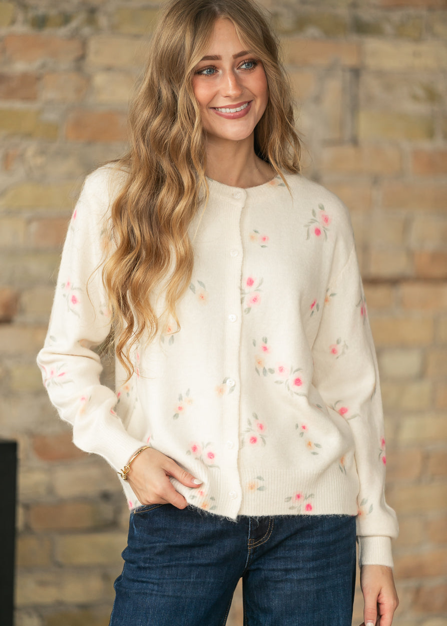 Front view of a model wearing a cream floral long sleeve knit cardigan with functional buttons