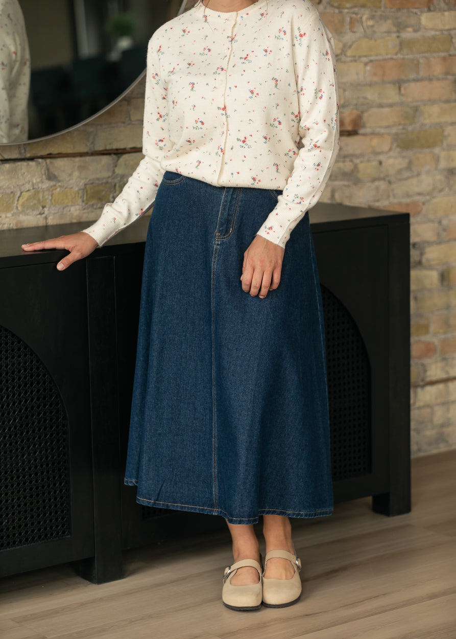 Dark indigo denim midi skirt with A-line silhouette styled with a cream floral cardigan and flats.