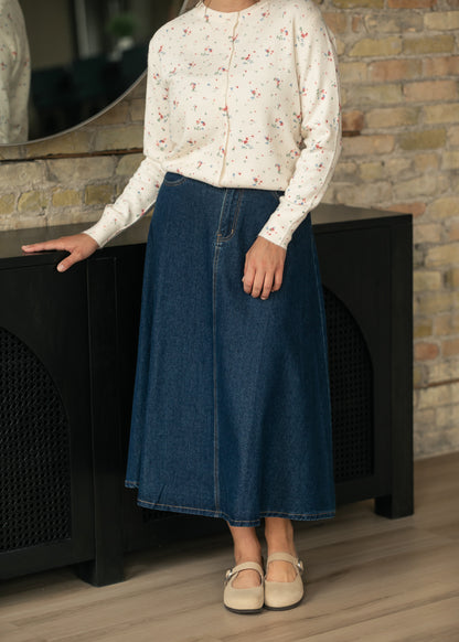Dark indigo denim midi skirt with A-line silhouette styled with a cream floral cardigan and flats.