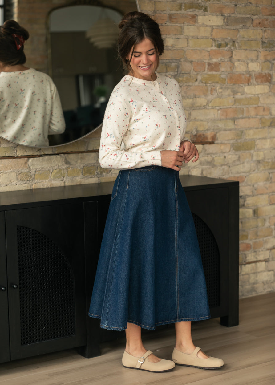 Side view of dark wash A-line denim midi skirt showing ankle-skimming movement and front pocket.
