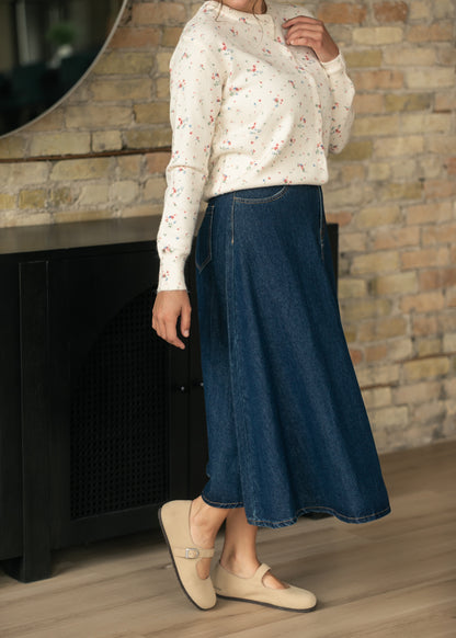 Dark indigo denim A-line midi skirt styled with a cream floral cardigan and neutral flats.