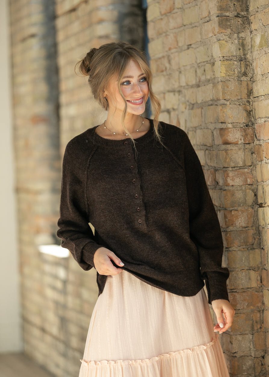 Dark brown henley sweater with a raw-edge collar, styled with a delicate layered necklace.