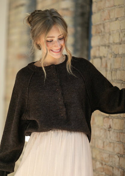 Dark brown henley sweater with a relaxed, cropped fit, styled with a flowing maxi skirt.