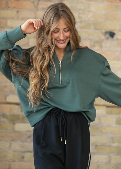 Dark forest quarter zip sweatshirt with a notched collar and gold-tone zip pull, paired with black track pants.