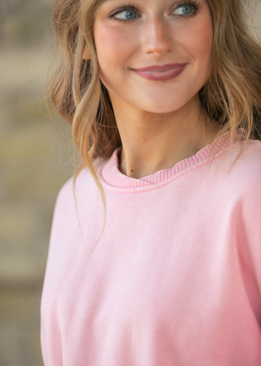 Close-up of a dusty pink fleece crewneck with a ribbed, raw-edge collar.