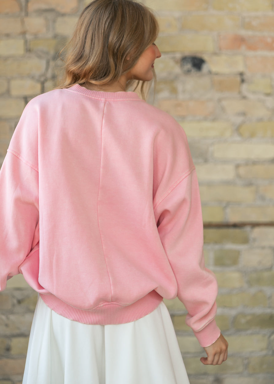 Back of a dusty pink fleece crewneck sweatshirt showing the ribbed hem and dropped shoulders.