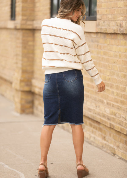 Back view of dark wash denim midi skirt with raw hem, styled with a cream striped sweater and brown wedges.