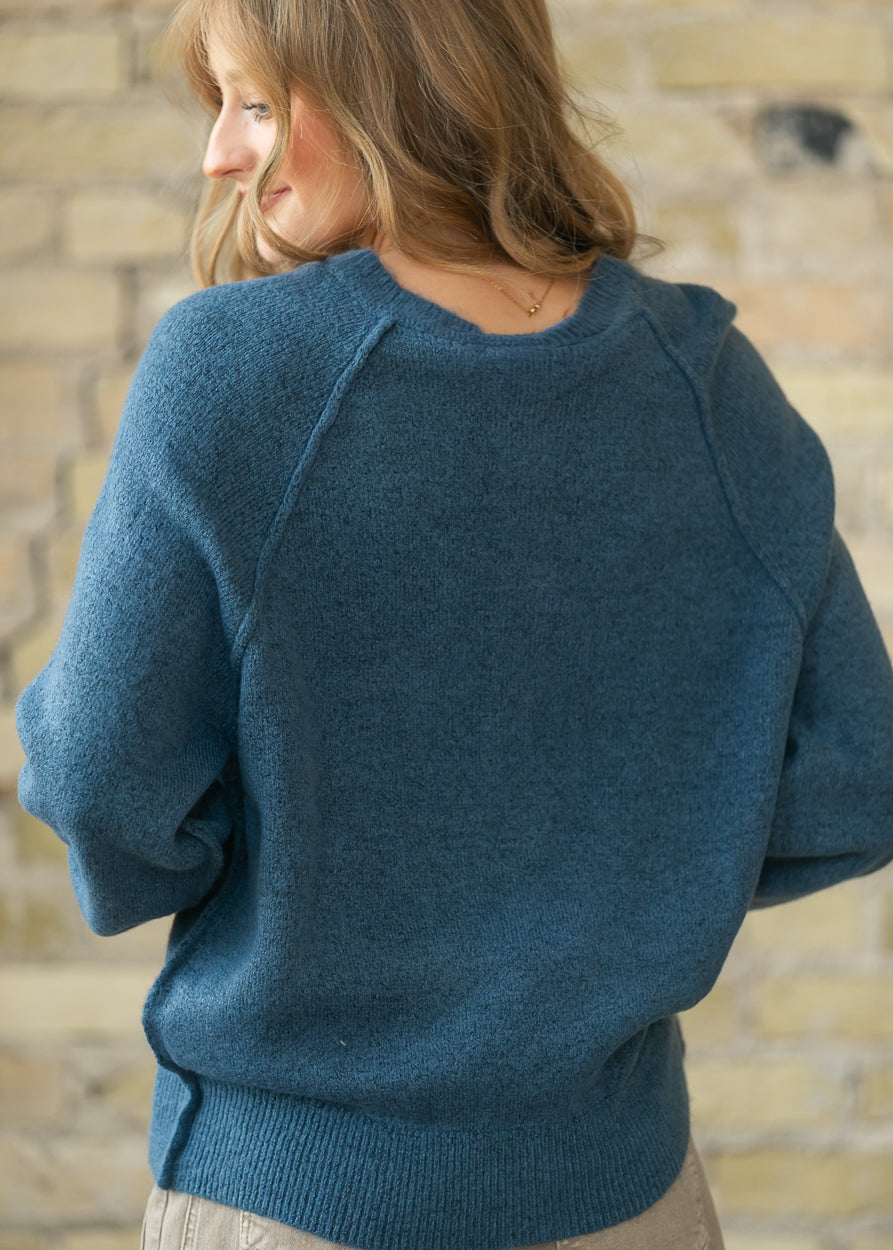 Back of the dusty blue henley sweater showing raglan sleeves and a relaxed fit.
