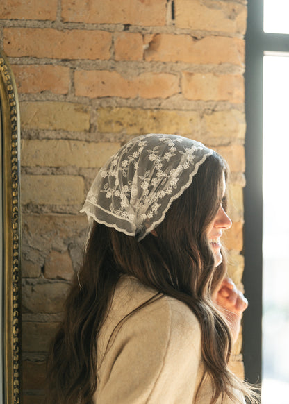 Ivory floral lace triangle scarf worn over the hair, showing scalloped edging and sheer embroidered detail.