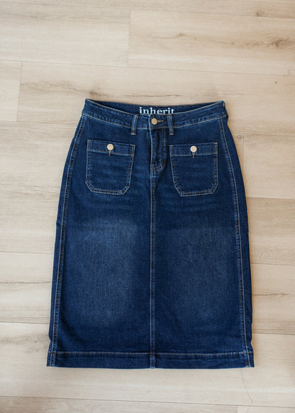 A dark blue denim skirt with front patch pockets and a visible 'inherit' brand label at the waistband, laid flat on a light wood floor.