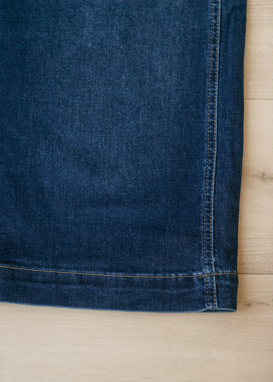 Close-up of a dark blue denim fabric corner with visible stitching, laid flat on a light wood surface.
