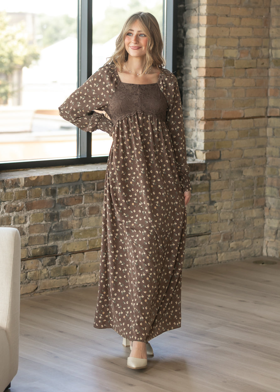 Brown floral maxi dress in a lifestyle setting, showing the square neckline, lace bodice, and long sleeves.