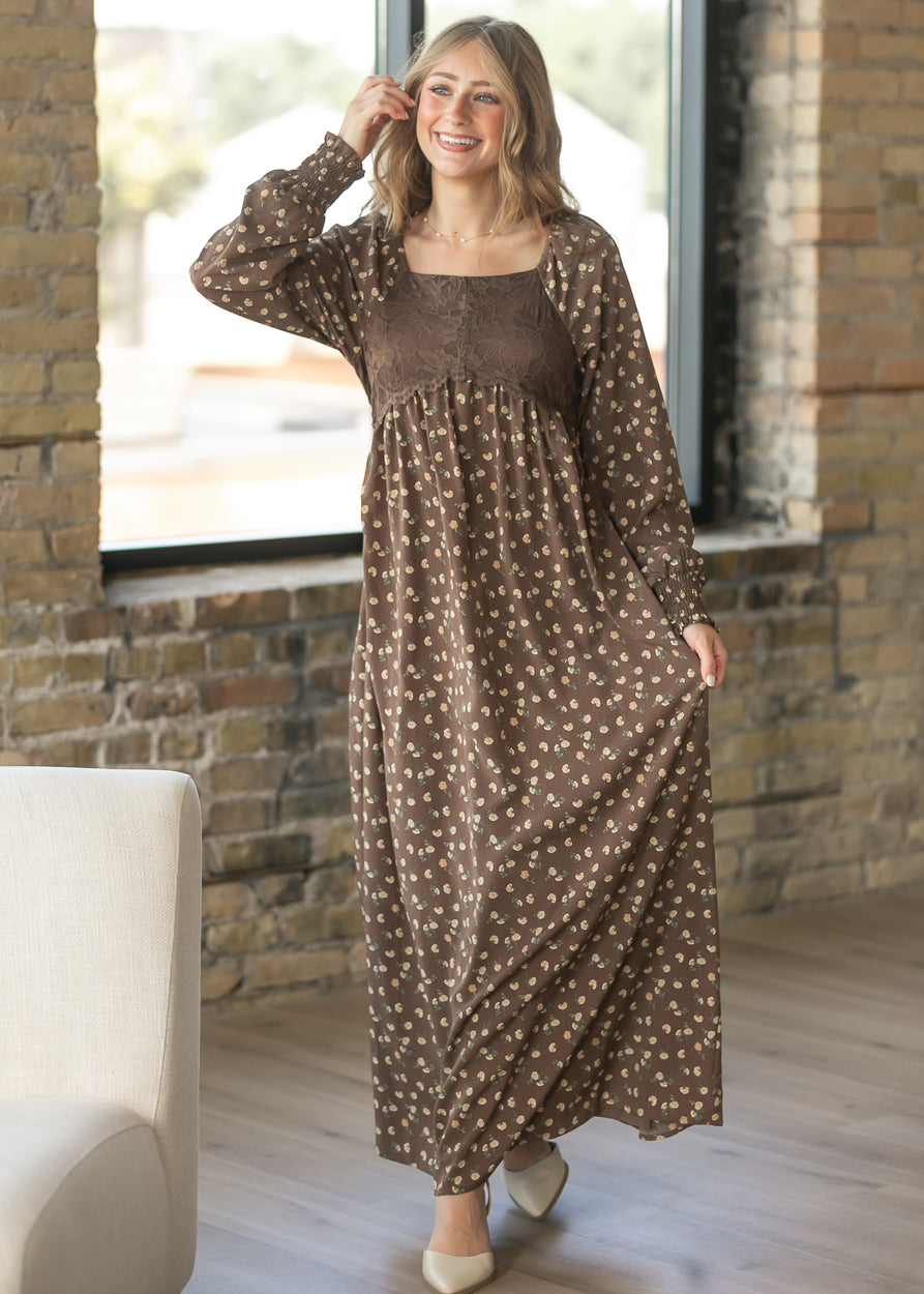 Elise brown floral maxi dress with lace bodice, long sleeves, and flowing skirt in a bright indoor setting.