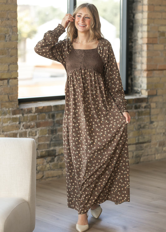 Elise brown floral maxi dress with lace bodice, long sleeves, and flowing skirt in a bright indoor setting.