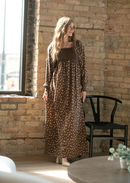 Elise brown floral maxi dress with lace bodice, long sleeves, and square neckline in a sunlit brick interior.