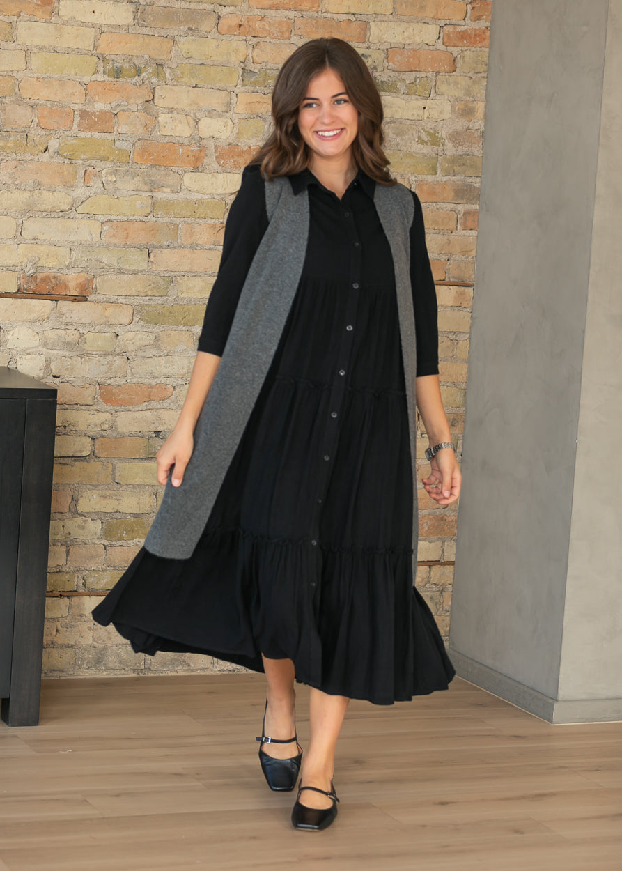 Black Elsie midi dress with half sleeves, button front, and tiered A-line skirt, styled indoors.