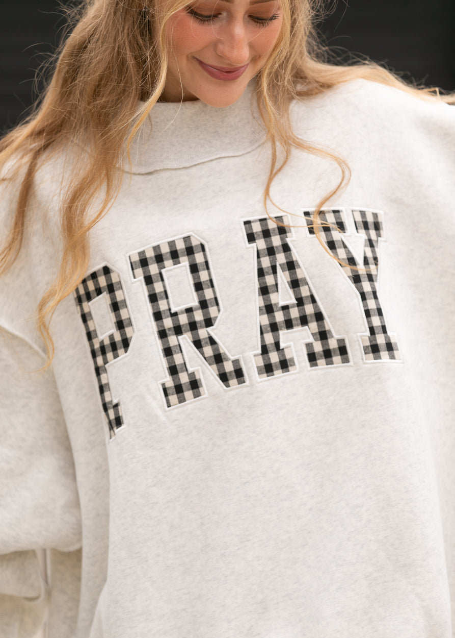 Close-up of gingham Pray lettering on oatmeal heather mockneck sweatshirt.