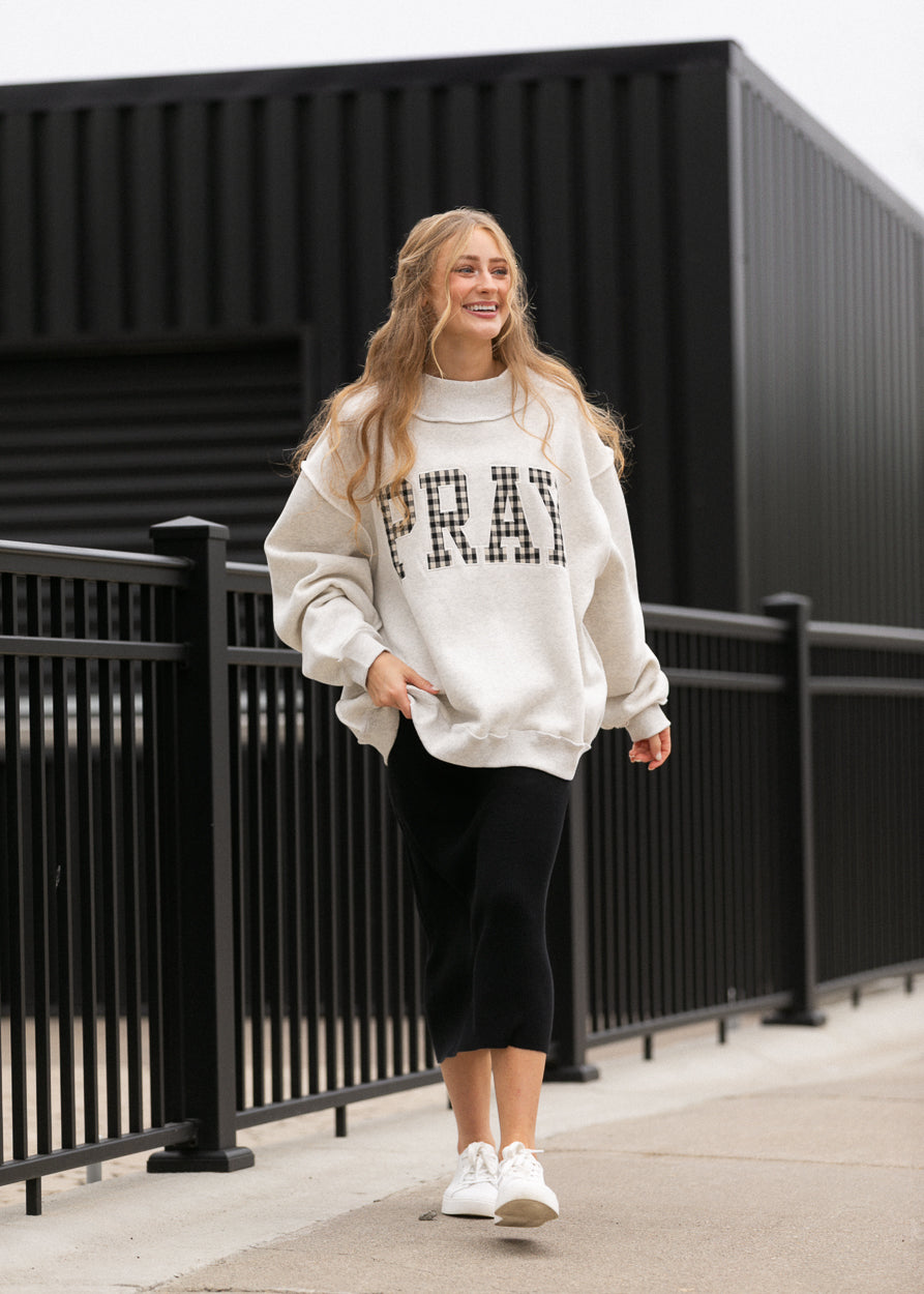 Oatmeal Pray mockneck sweatshirt styled with a black midi skirt and white sneakers.