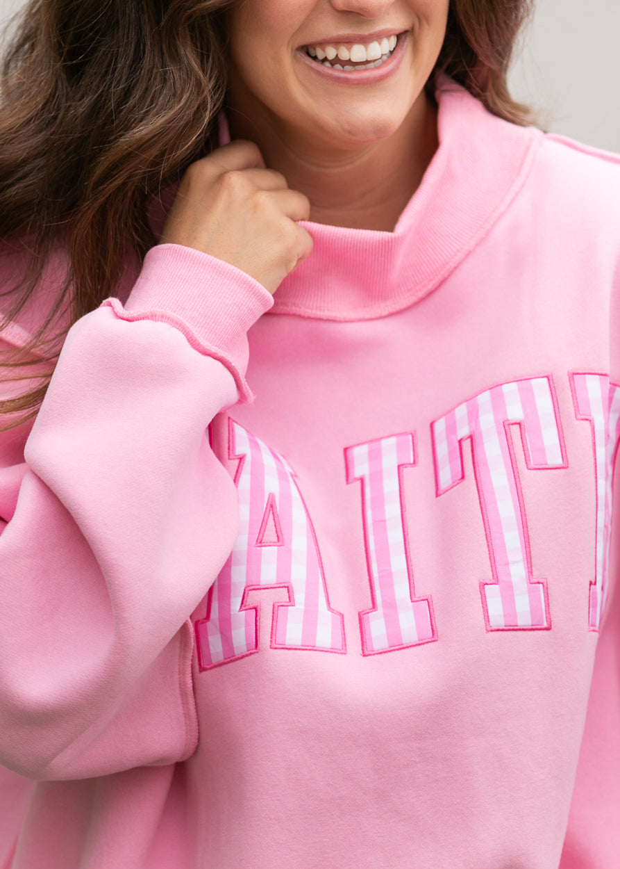 Close-up of pink-and-white gingham Faith lettering on bright pink mockneck sweatshirt.